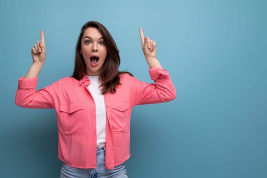 shocked black haired lady in casual style pointing finger at wall in studio background.