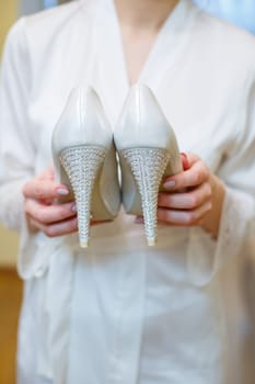 White shoes with heels in the hands of the bride