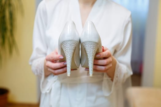 White shoes with heels in the hands of the bride
