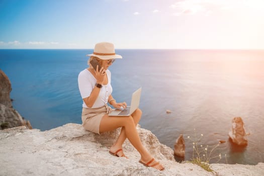 Freelance women sea. She is working on the computer, talking on the phone in the open air with a beautiful view of the sea. The concept of remote work