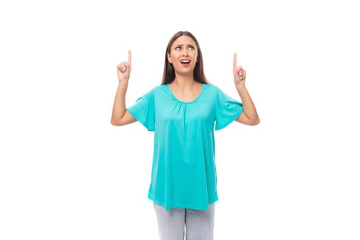 young brunette european lady with straight hair dressed in a blue t-shirt points her hands up at the ceiling.