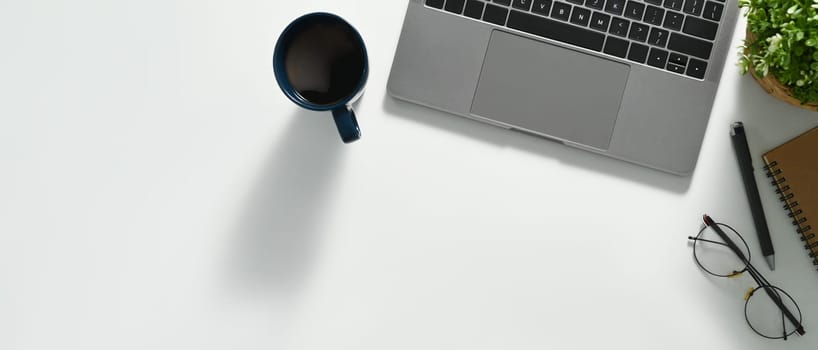 A cup of coffee, laptop, glasses and notebook on white office desk. Top view with coy space.