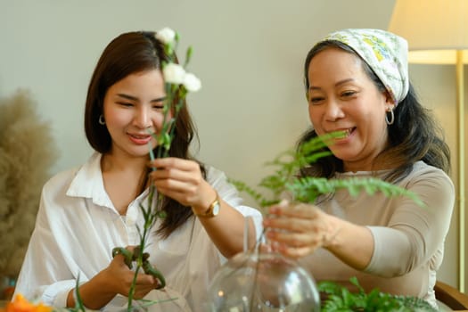 Joyful senior woman and adult daughter creating beautiful bouquet in living room. Family and leisure activity concept.