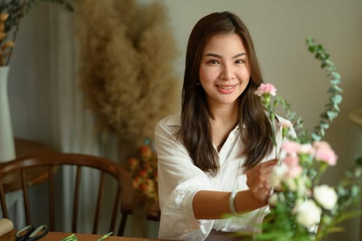 Attractive woman making a bouquet with fresh flowers at floral shop. Retirement, floristry and small business concept.