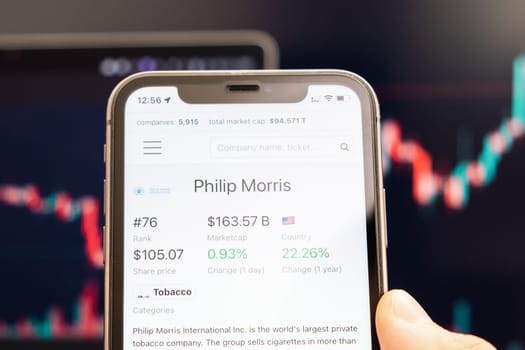 Philip Morris stock price on the screen of cell phone in mans hand with changing stock market exchange with trading candlestick graph analysis, February 2022, San Francisco, USA