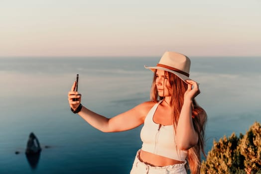 Selfie woman in hat, white tank top and shorts makes selfie shot mobile phone post photo social network outdoors on sea background beach people vacation lifestyle travel concept