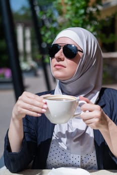 Caucasian woman in hijab drinking coffee in outdoor cafe