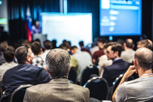 Speaker giving a talk in conference hall at business event. Rear view of unrecognizable people in audience at the conference hall. Business and entrepreneurship concept