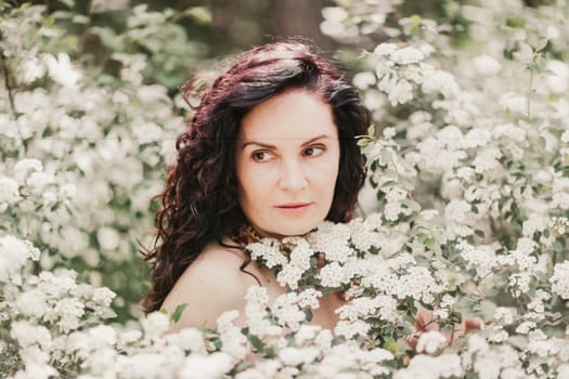 Woman spirea flowers. Portrait of a curly happy woman in a flowering bush with white spirea flowers