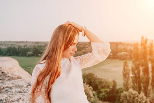 Romantic beautiful bride in white dress posing with sea and mountains in background. Stylish bride standing back on beautiful landscape of sea and mountains on sunset