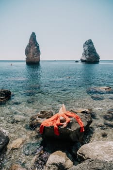 Woman travel sea. Young Happy woman in a long red dress posing on a beach near the sea on background of volcanic rocks, like in Iceland, sharing travel adventure journey