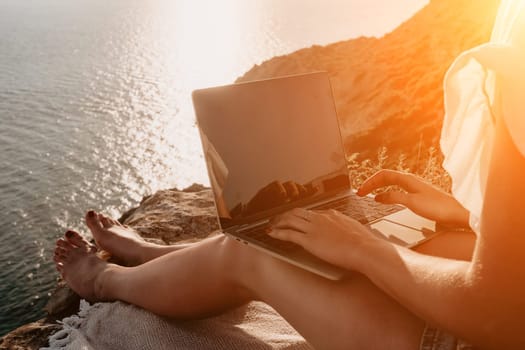 Woman sea laptop. Business woman in yellow hat working on laptop by sea. Close up on hands of pretty lady typing on computer outdoors summer day. Freelance, digital nomad, travel and holidays concept.