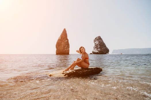 Woman travel sea. Young Happy woman in a long red dress posing on a beach near the sea on background of volcanic rocks, like in Iceland, sharing travel adventure journey