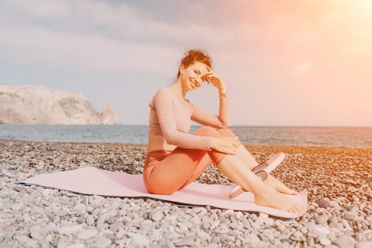 Middle aged well looking woman with black hair doing Pilates with the ring on the yoga mat near the sea on the pebble beach. Female fitness yoga concept. Healthy lifestyle, harmony and meditation.