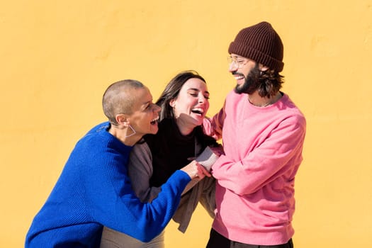 group of three friends laughing and joking around on yellow background, concept of friendship and happiness, copy space for text