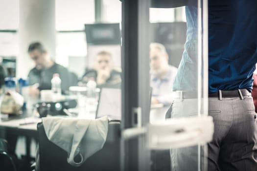 Business man making a presentation at office. Business executive delivering a presentation to his colleagues during meeting or in-house business training. View through glass.