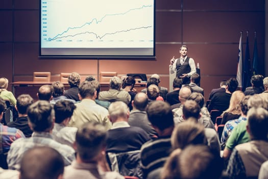 Speaker giving a talk in conference hall at business meeting event. Rear view of unrecognizable people in audience at the conference hall. Business and entrepreneurship concept.