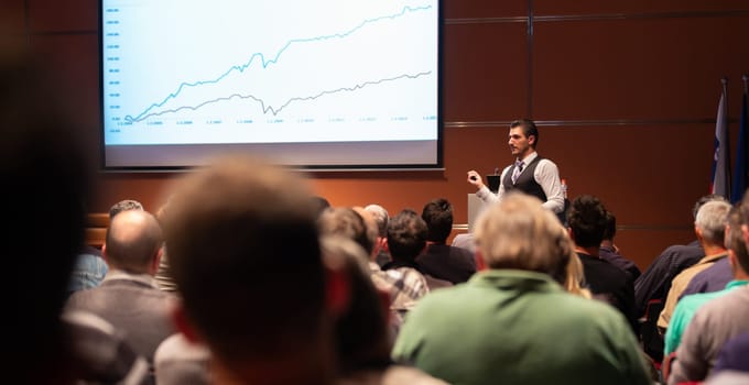 Speaker giving a talk in conference hall at business meeting event. Rear view of unrecognizable people in audience at the conference hall. Business and entrepreneurship concept.