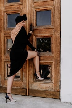 Stylish woman in the city. Fashion photo of a beautiful model in an elegant black dress posing against the backdrop of a building on a city street.