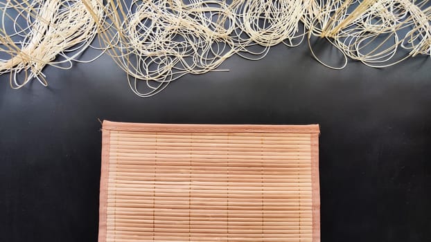 Asian bamboo mat and napkin from yellow bamboo on black surface. Background, texture, frame, copy space. Location for photo shoot