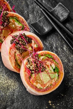 Closeup of rolls with crab meat, avocado, lettuce and orange slice wrapped in tuna, japanese omelette and soy bean paper mamenori without rice garnished with black tobiko sprinkled with golden powder