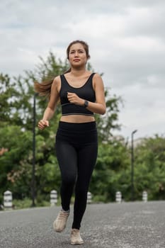 Happy woman wearing sportswear jogging in the park. Young beautiful asian female in sports bra running outdoor. Workout exercise in the morning. Healthy and active lifestyle concept.