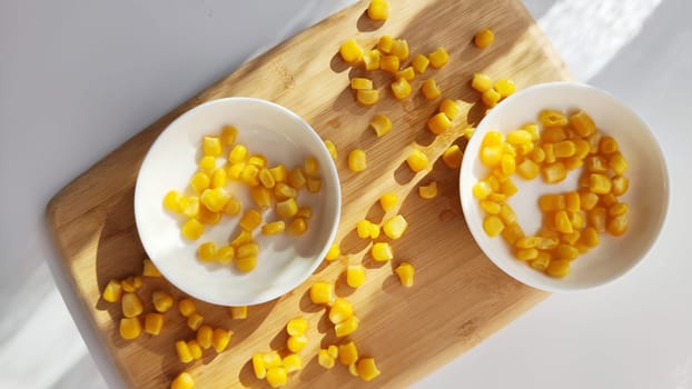 Lot of pieces of canned yellow corn on plate which is on wooden bamboo cutting board on white background. Concept of cooking and delicious healthy food