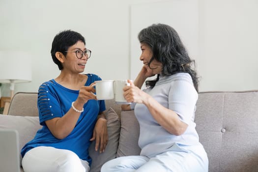 Elderly women drinking coffee while sitting on sofa at home.