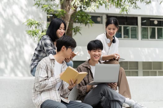 University students sitting together at table with books and laptop and tablet. Happy young people doing group study in university.