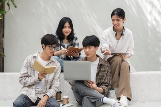 Group of happy students checking results on laptop and tablet while sitting on college campus, concept of education, technology and project work discussion.