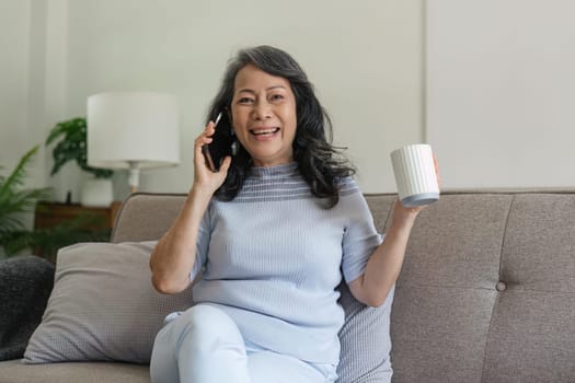 Portrait of stylish attractive mature sixty year old female with sitting in talking on the phone and white glass and drinking tea.