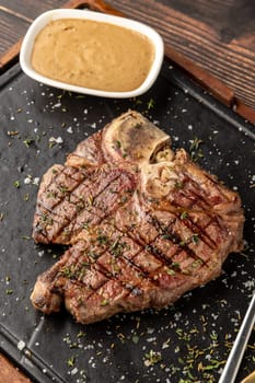 Top view of T-Bone Steak served on stone plate with sauce on the side