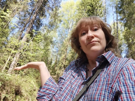 The blonde girl tourist takes selfie in nature in the forest on a hike or trip. The pretty woman poses while traveling in the summer, spring, or fall
