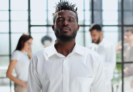 Portrait of smiling African American business man with executives working on laptop in background.