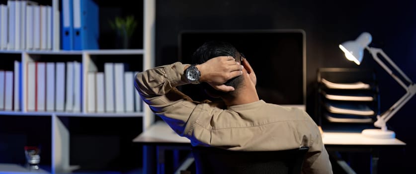 Overworked young Asian office employee working on laptop computer overtime in office at night.