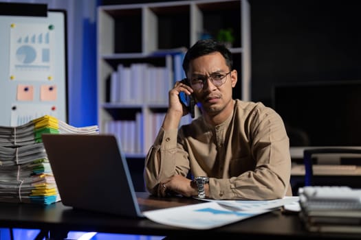 Overworked young Asian office employee working on laptop computer overtime in office at night.