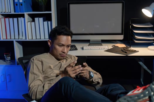 Overworked young Asian office employee working on laptop computer overtime in office at night.