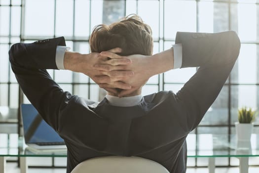 the worker sits in the office with his hands behind his head and looks out the window