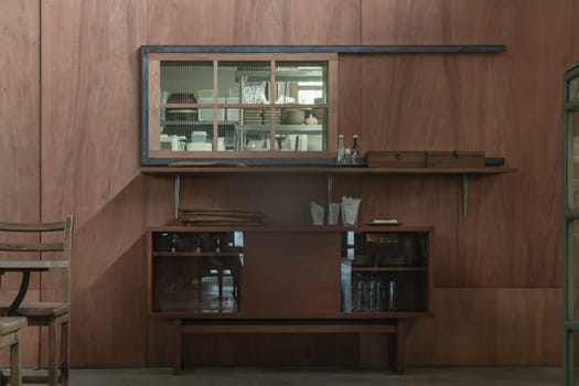 The Wooden Vintage Cabinet for Storing Dishes is placed in front of the Wooden Wall, which is outside of the Kitchen Counter. The Japanese Minimalist Restaurant Interior Design. Selective focus.