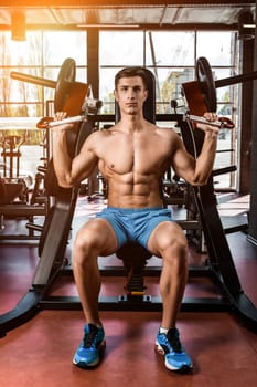 Tense muscles of hands under load. Man doing exercise for biceps in the gym. Work on tell muscles on the simulator. Photos for sporting magazines, posters and websites. sun flare