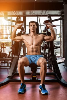 Tense muscles of hands under load. Man doing exercise for biceps in the gym. Work on tell muscles on the simulator. Photos for sporting magazines, posters and websites. sun flare