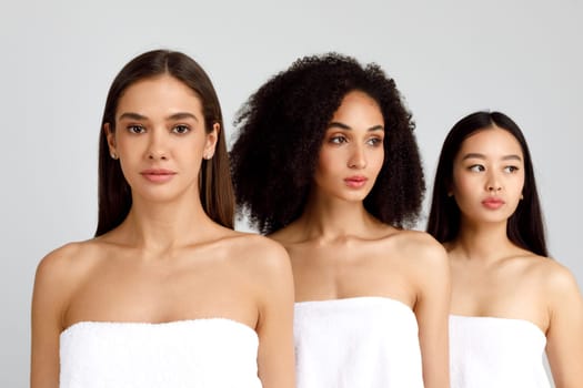 Youth and beauty concept. Three young multiracial ladies posing wrapped in towels over grey studio background. Beautiful women with perfect smooth skin and nude makeup, banner