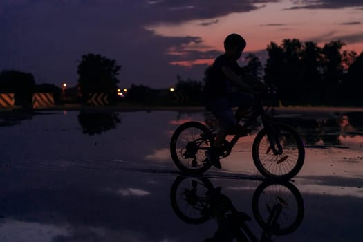 Lonely children silhouette on bike, boy riding bicycle on reflective water. Background beautiful sunset. High quality photo