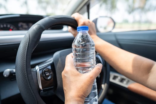 Asian woman driver holding bottle for drink water while driving a car. Plastic hot water bottle cause fire.