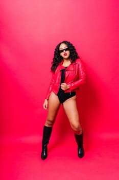 African American curvy female in black bodysuit and jacket on red and white background in a studio