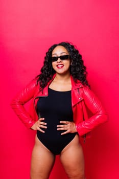 African American curvy female in black bodysuit and jacket on red and white background in a studio