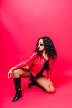 African American curvy female in black bodysuit and jacket on red and white background in a studio