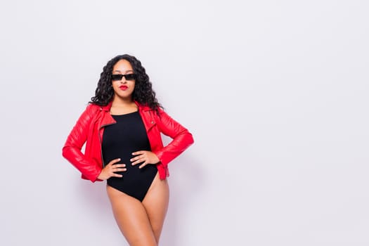 African American curvy female in black bodysuit and jacket on red and white background in a studio