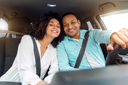 Car Owners. Happy middle eastern family husband and wife enjoying automobile ride together on weekend, leaning to each other posing with safety belts on, smiling at camera