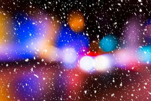 Blurred lights of headlights of cars and lanterns in the night city in a snowfall. Abstract bright bokeh.